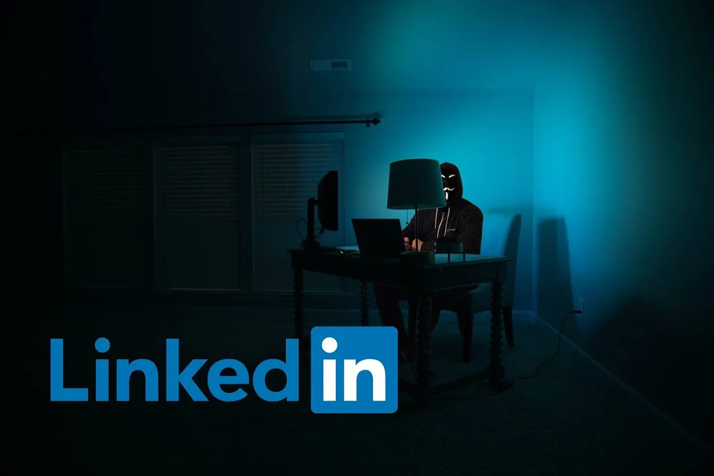 A hooded figure at a desk in a dark room with a LinkedIn logo overlay.